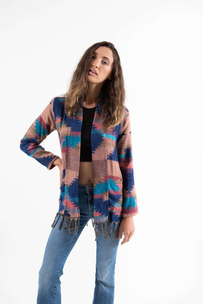 Brunette woman wearing blue and coral colored bohemian fringe cardigan sweater.